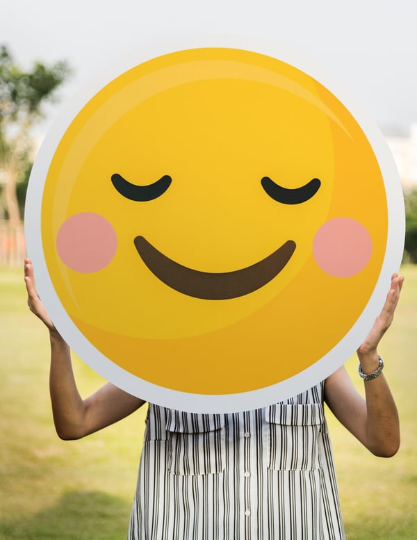 A Person in a Striped Top Holding a Yellow Smiling Face Emoji in Front of their Face