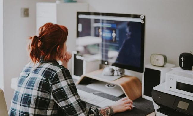  A Woman Sat Down and Looking at a Desktop Whilst Holding a Computer Mouse