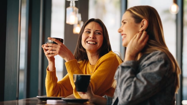 Two friends chatting in a cafe while holding a coffee