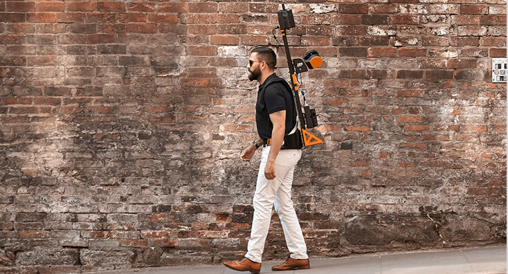 Man Walking and Carrying Scanning Equipment next to a Brick Wall