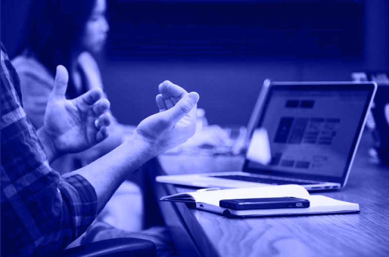 Blue Image of a Person Discussing a Topic using a Notepad and a Laptop