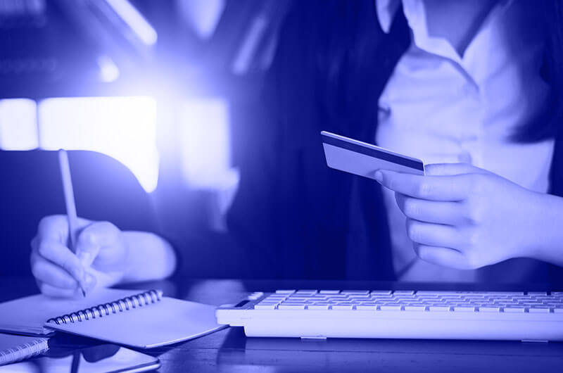 Blue Image of a Woman Holding a Bank Card and Writing in a Notebook