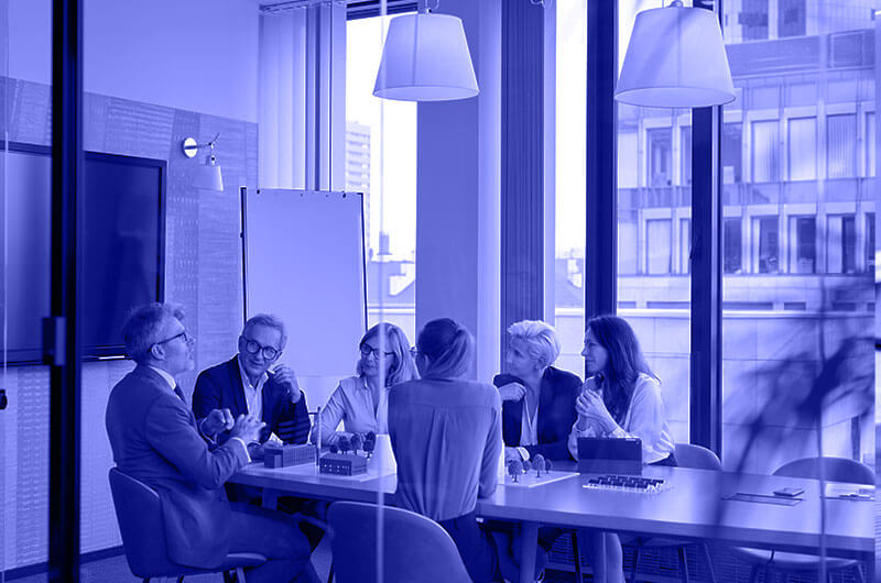 Blue Image of Six People Sat Down at a Table in a Meeting