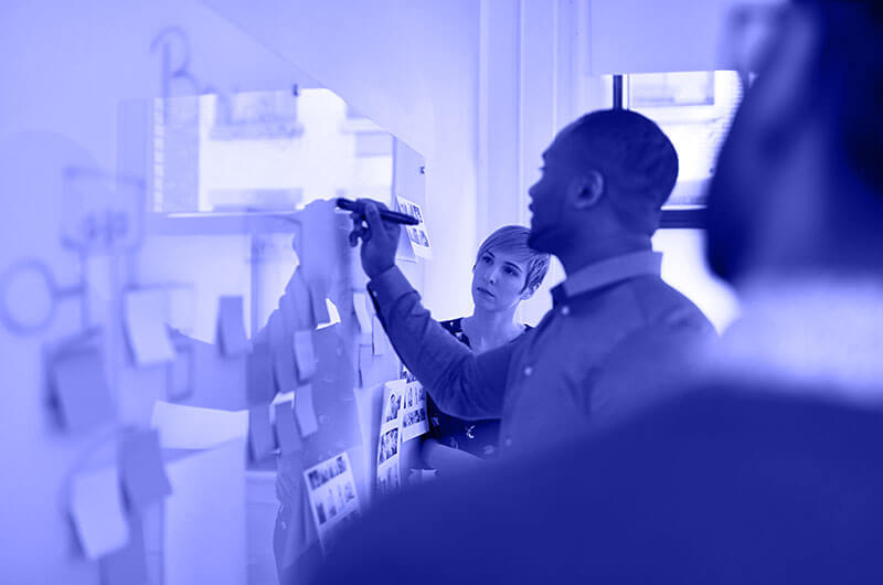 Blue Image of a Man Writing on a Whiteboard with a Woman Watching