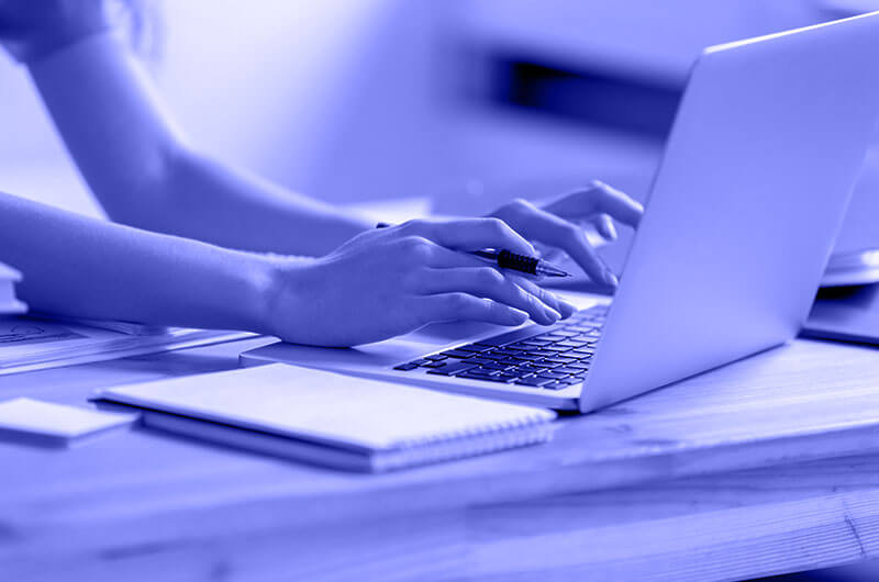 Blue Image of a Person Typing on a Laptop at a Table