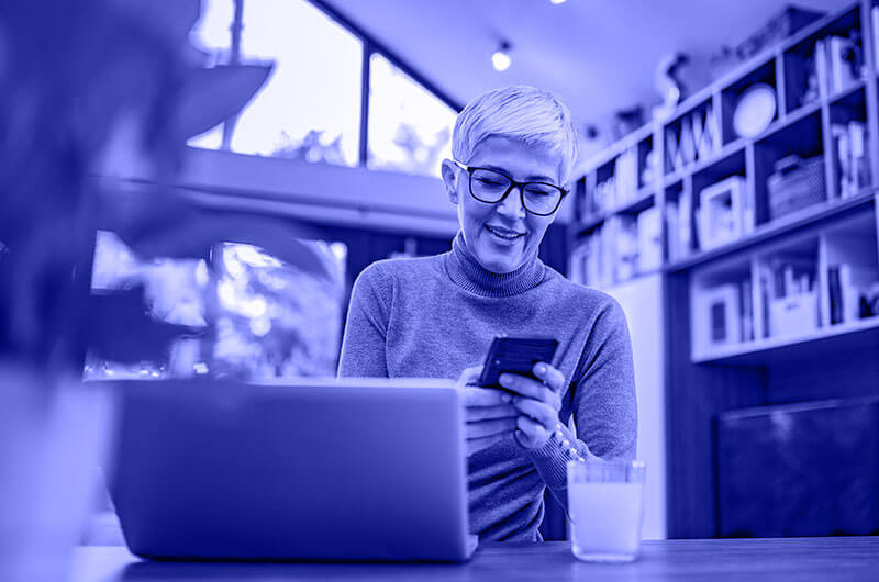 Blue Image of a Woman using her Phone and Laptop at a Table