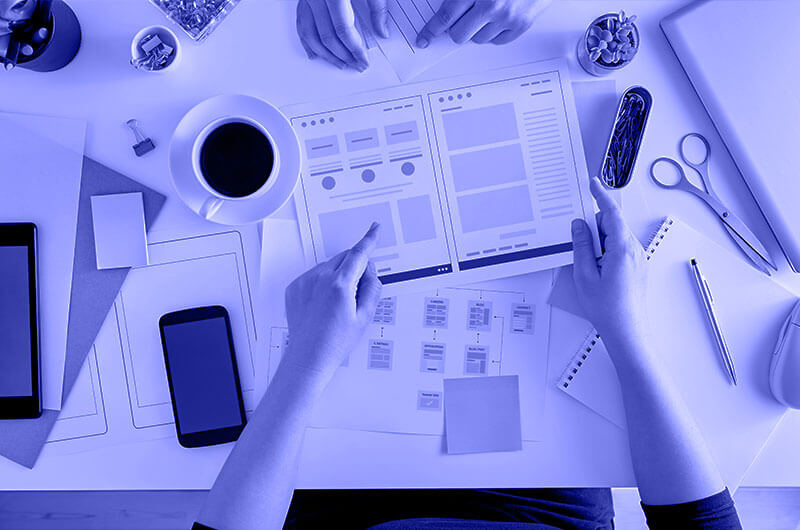Blue Image of Two People Working on a Website Plan at a Desk