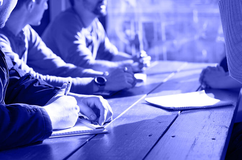 Blue Image of People Talking to Each Other and Writing Notes at a Table