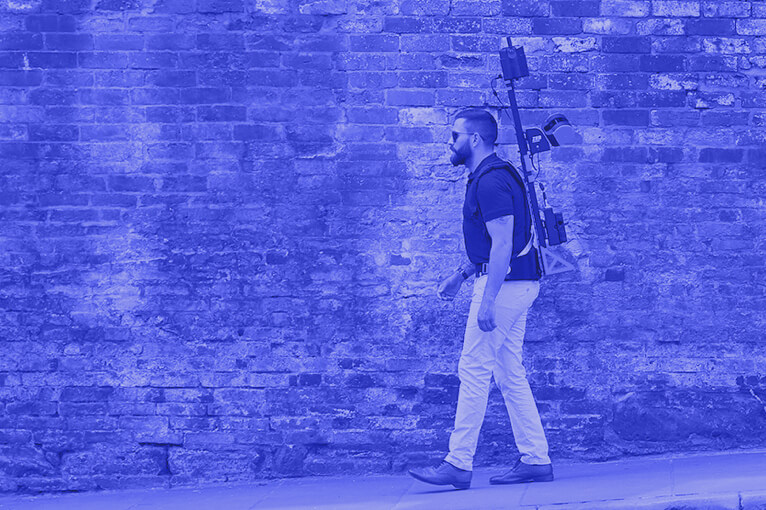 Blue Image of a Man Walking and Carrying Building Scanning Equipment
