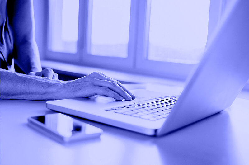 Blue Image of a Person Scrolling on a Laptop at a Table