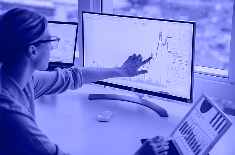 Blue Image of a Woman Pointing to Graphs on a Tablet and a Computer