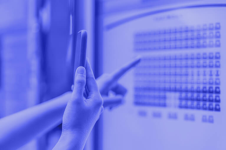 Blue Image of a Person Pointing at a Computer Screen and Holding a Phone