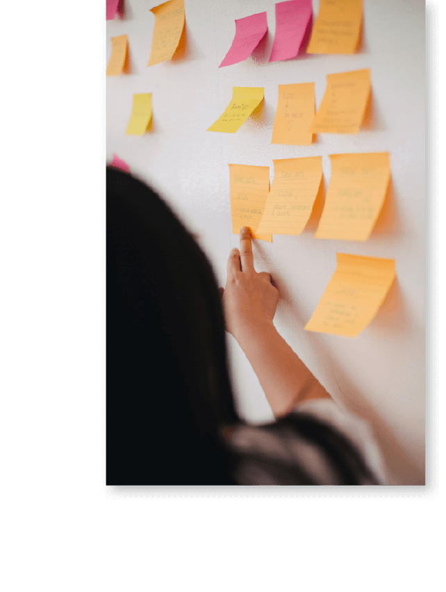 Woman Pointing at and Reading from Orange and Pink Post It Notes