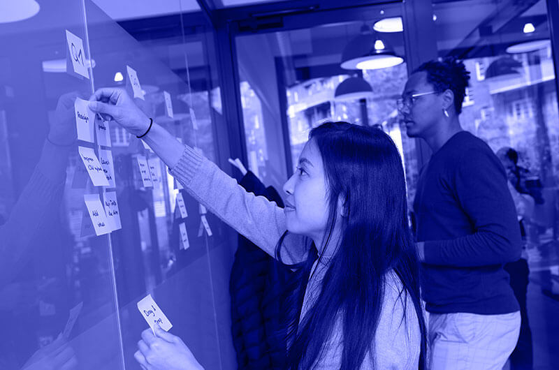 Blue Image of a Man and Woman Sticking Post It Notes on a Board