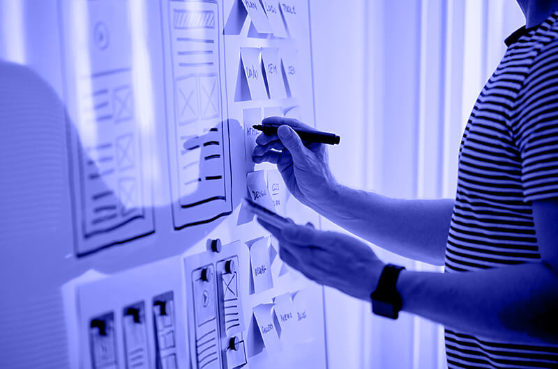 Blue Image of a Person Writing on a Whiteboard and Post It Notes